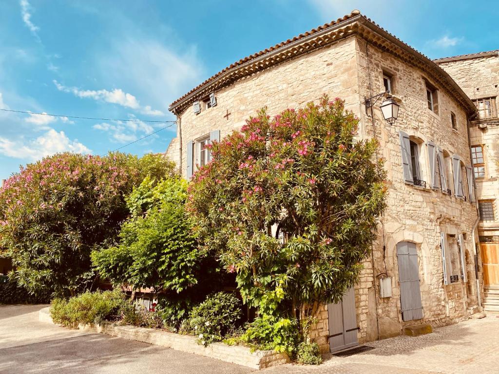 un edificio de piedra con un árbol delante de él en Les Lauriers Roses - Maison d'Hôtes, en Barjac