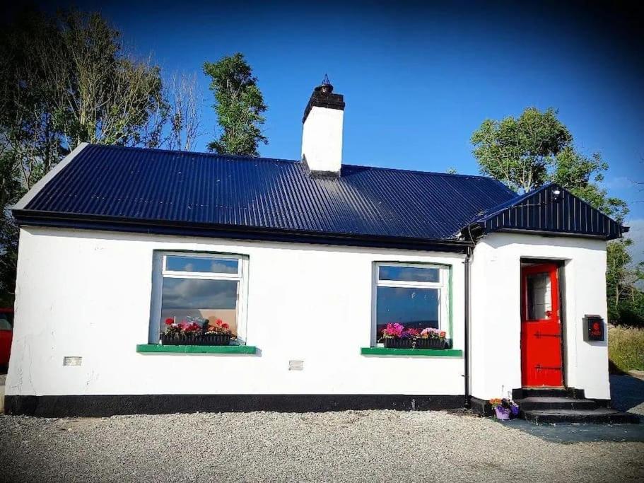 ein weißes Haus mit zwei Fenstern und einer roten Tür in der Unterkunft Mary Grays Hideaway 2 Bedroom Irish Cottage 