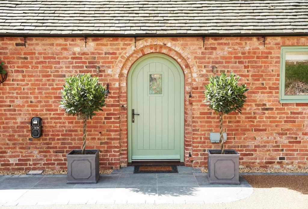 a brick house with a green door and two potted plants at Woodland Retreat in Burton upon Trent