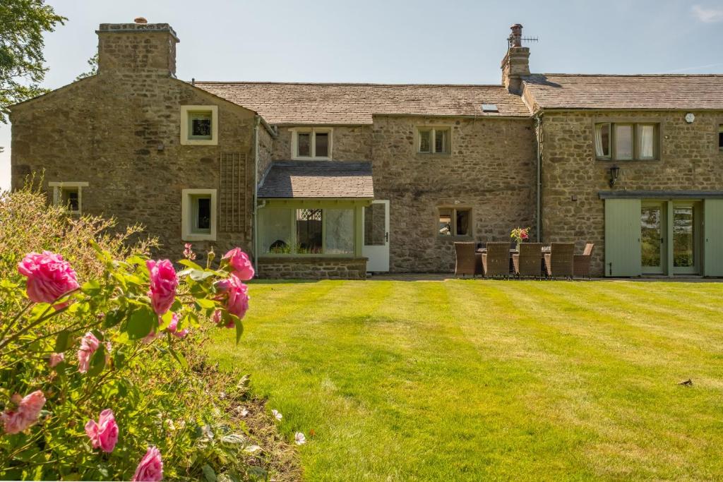 uma grande casa de pedra com um quintal com flores cor-de-rosa em Masongill Lodge em Cowan Bridge
