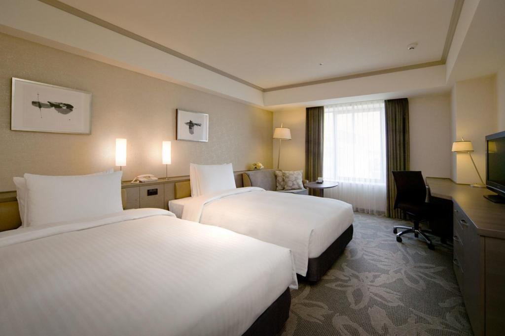 a hotel room with two beds and a desk at Hotel Nikko Fukuoka in Fukuoka