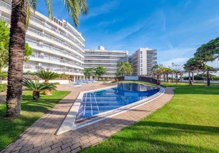 a large building with a swimming pool in a park at S'Abanell Central Park seafront apartment in Blanes