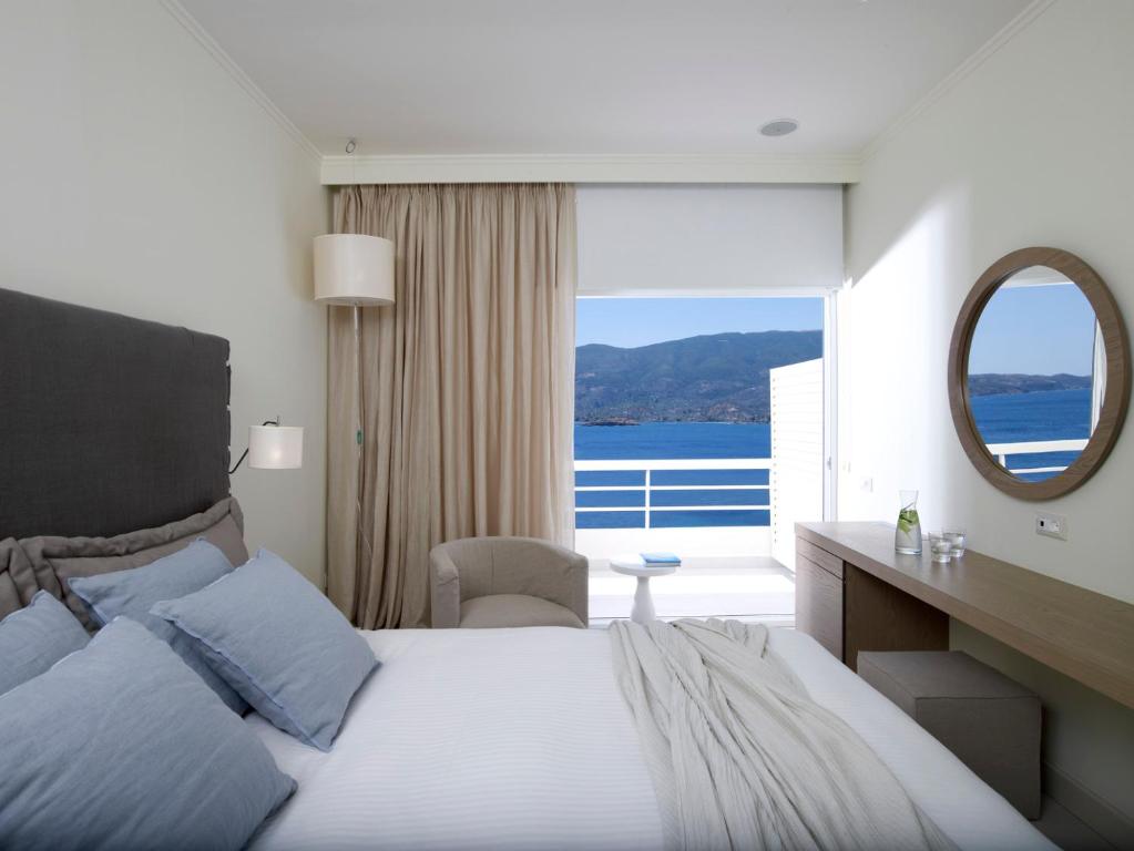 a bedroom with a large bed and a mirror at Sirene Blue Luxury Beach Resort in Poros