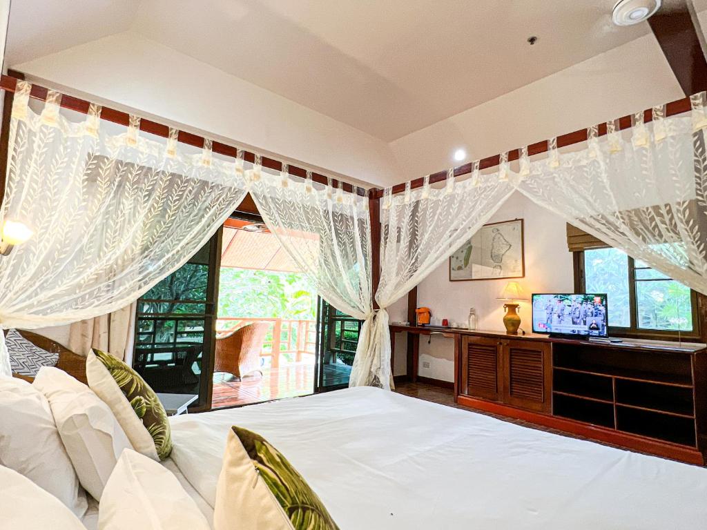 a bedroom with a bed with white curtains and a tv at Cruiser Island By Swiss-Belhotel in Ko Lone