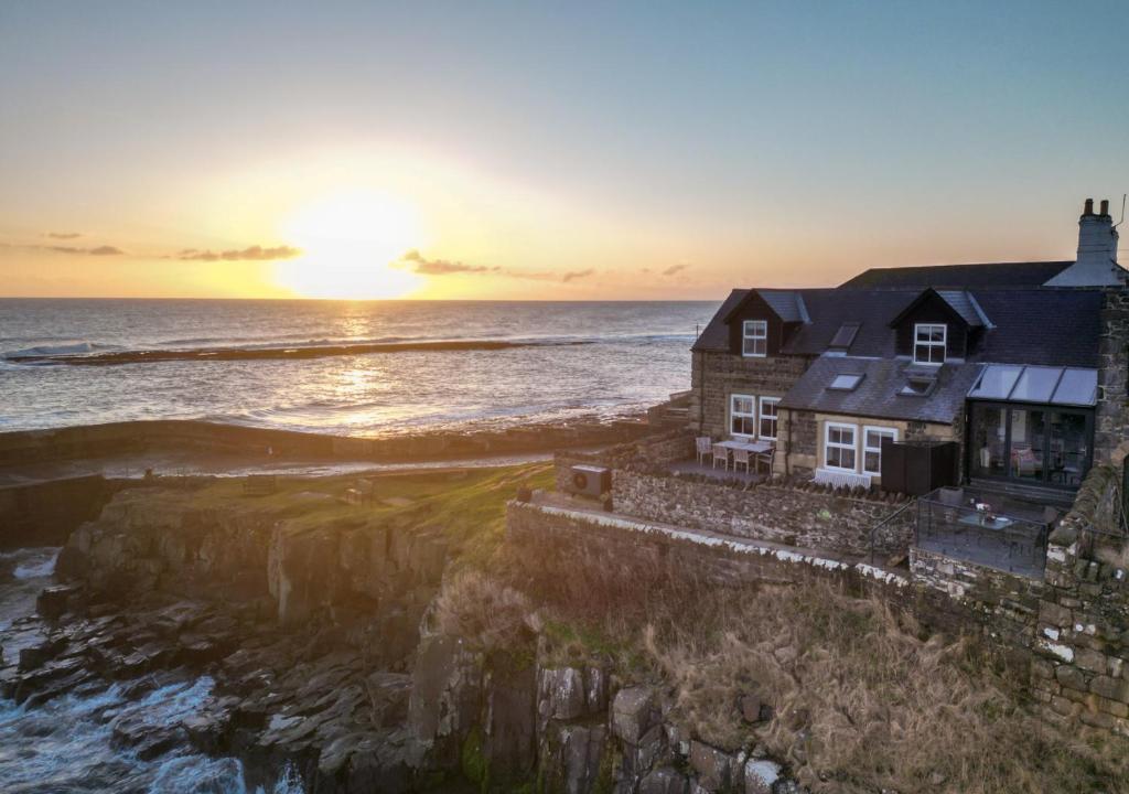 a house on the shore of the ocean at sunset at Harbour Masters House in Craster
