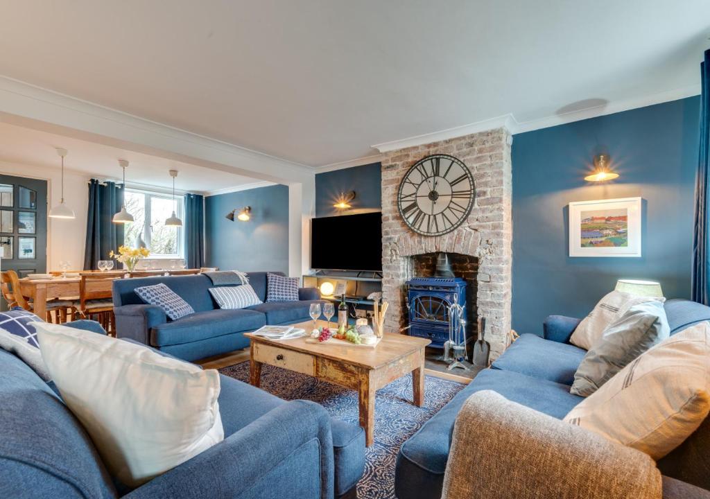 a living room with blue furniture and a clock on the wall at Coastguard Cottage in Craster