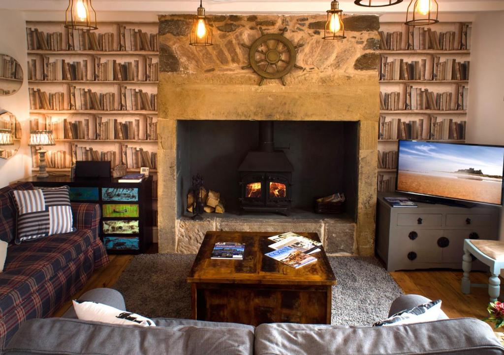 a living room with a fireplace and a couch and a tv at The Old Ale House in Craster