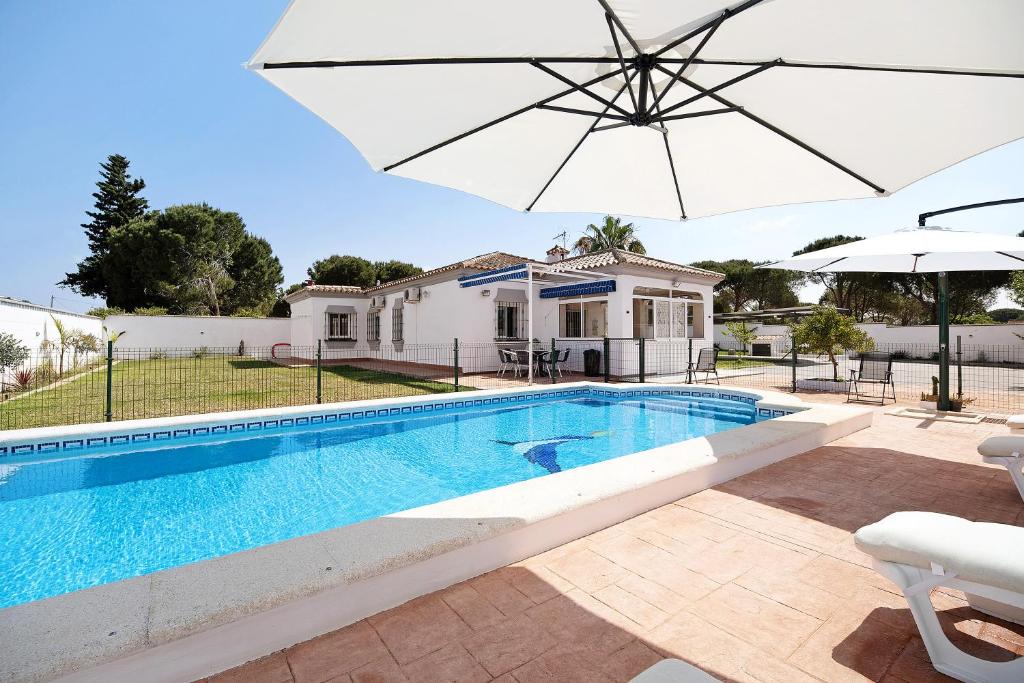 a swimming pool in front of a house with an umbrella at Villa Manuel in Chiclana de la Frontera