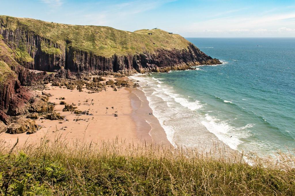 una playa con un grupo de personas de pie en la arena en Manorbier House - Lundy North Room, en Tenby