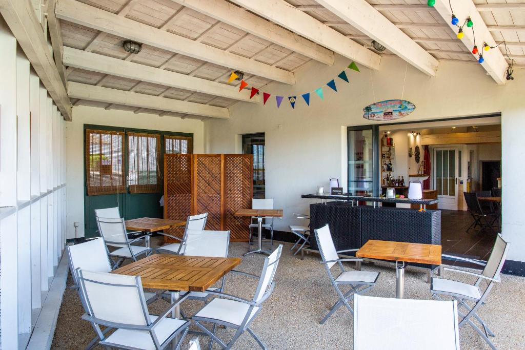 d&#39;une terrasse avec des tables en bois et des chaises blanches. dans l&#39;établissement Hôtel Les Vignes de la Chapelle, &quot;The Originals Relais&quot;, à Sainte-Marie de Ré