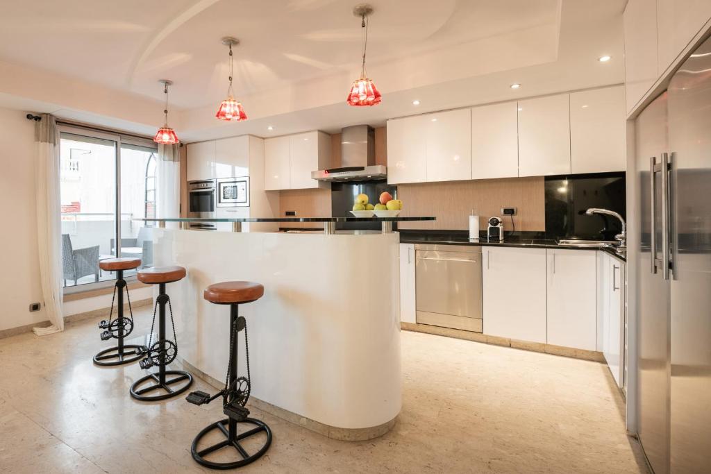 une cuisine avec des armoires blanches et des tabourets de bar dans l'établissement Chauvain Résidence, à Nice