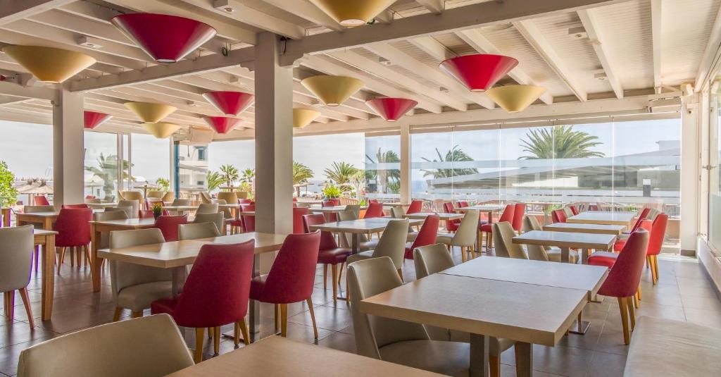 a restaurant with tables and red chairs and windows at ILUNION Costa Sal Lanzarote in Puerto del Carmen