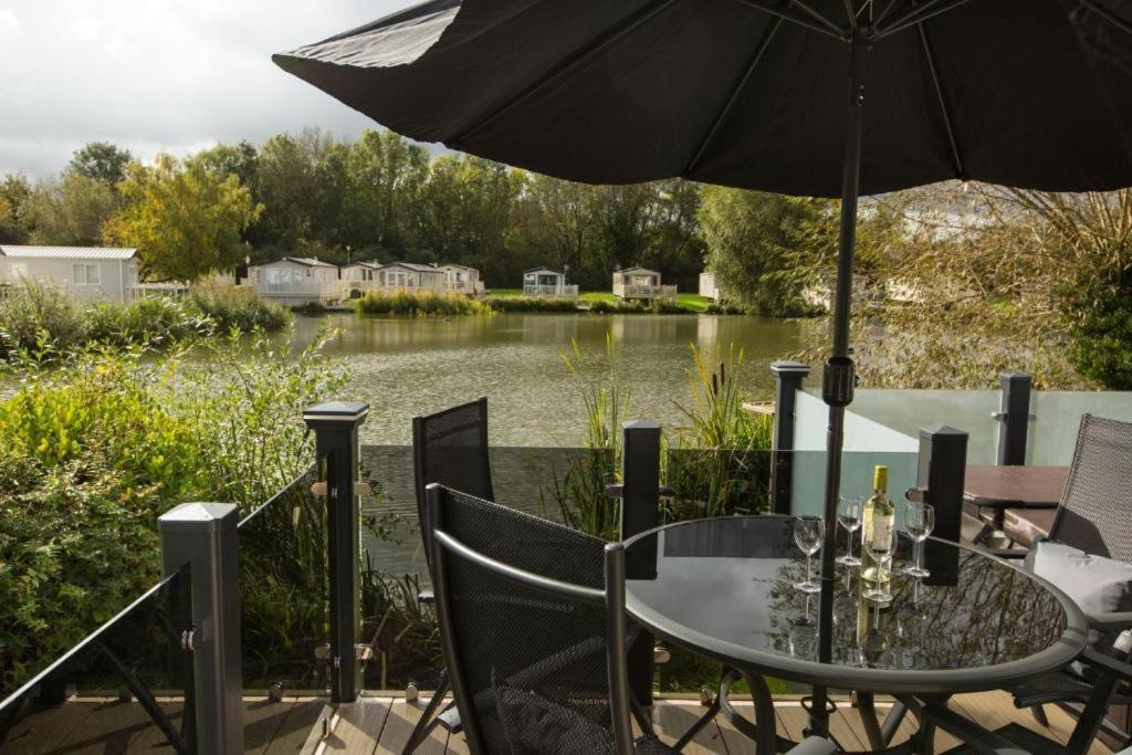 a table and chairs with an umbrella and a lake at Mallard Lake in South Cerney