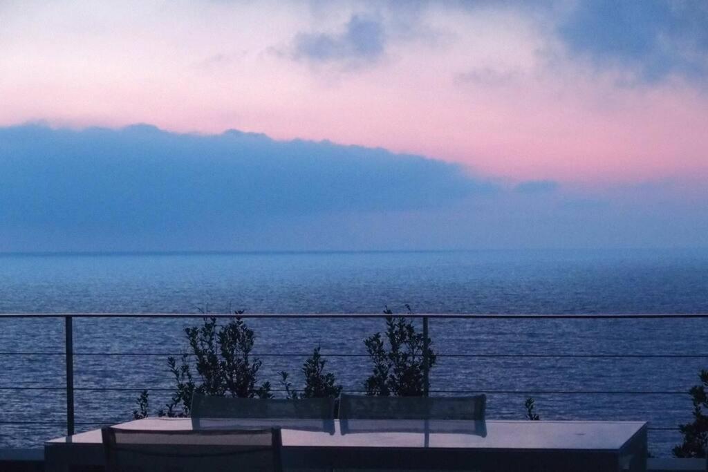una vista del océano al atardecer con dos bancos en Belle villa avec vue sur mer d'exception- Meria, en Meria