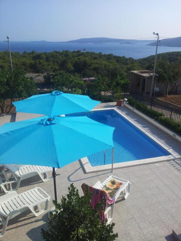 a blue umbrella and chairs next to a swimming pool at Apartment M in Seget Vranjica