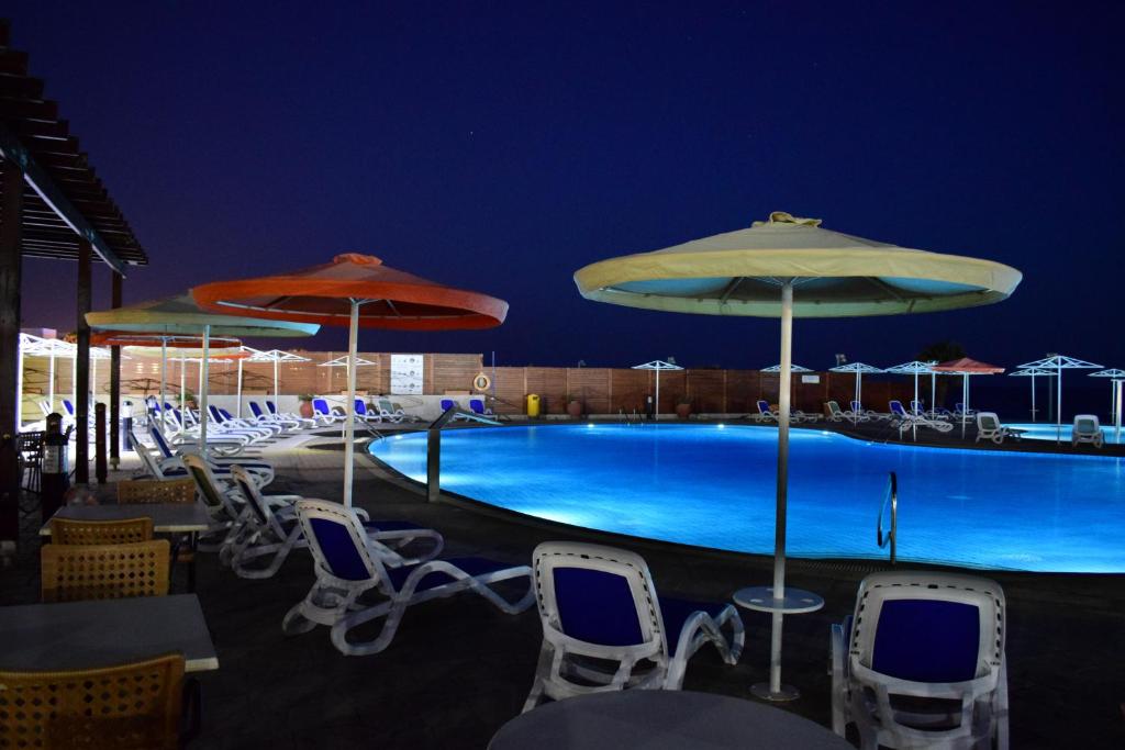 a swimming pool with chairs and umbrellas at night at Aktea Beach Village in Ayia Napa