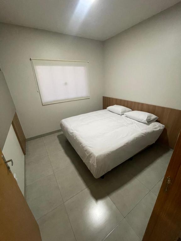 a bedroom with a white bed with a window at Vêneto Flat Residence (AP-13) in Primavera do Leste
