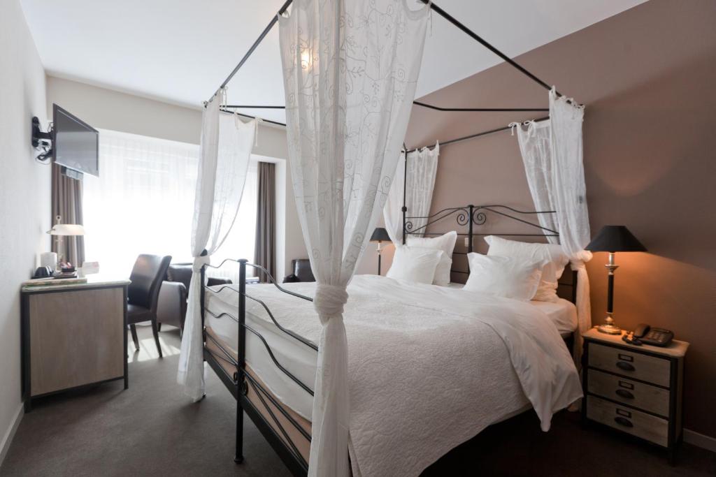 a bedroom with a canopy bed with white bedding and a desk at Hotel De Hofkamers in Ostend