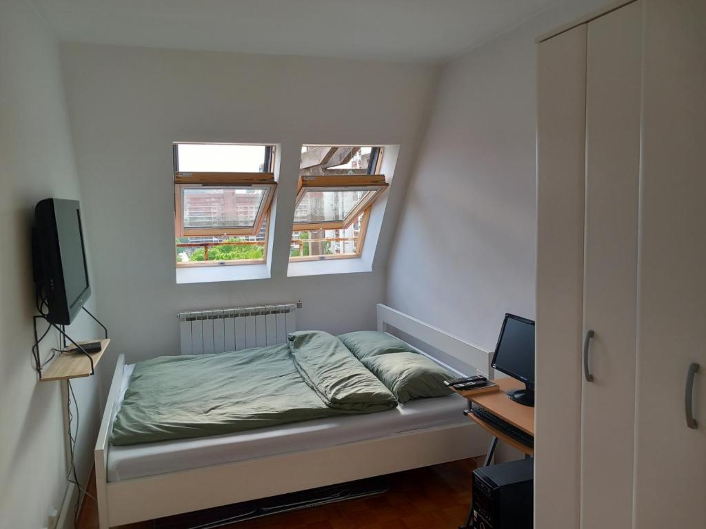 a bedroom with a bed and a desk and two windows at Apartment 075 in Tuzla
