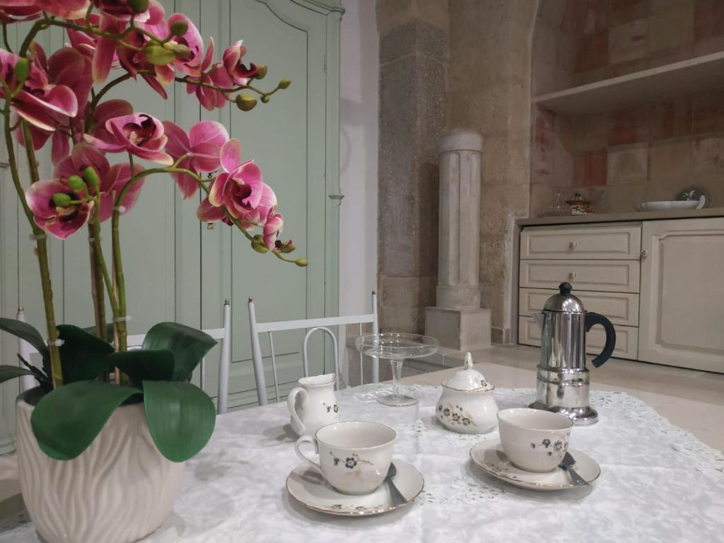 una mesa con un jarrón de flores rosas y tazas de té en La Sorgente B&B, en Trani