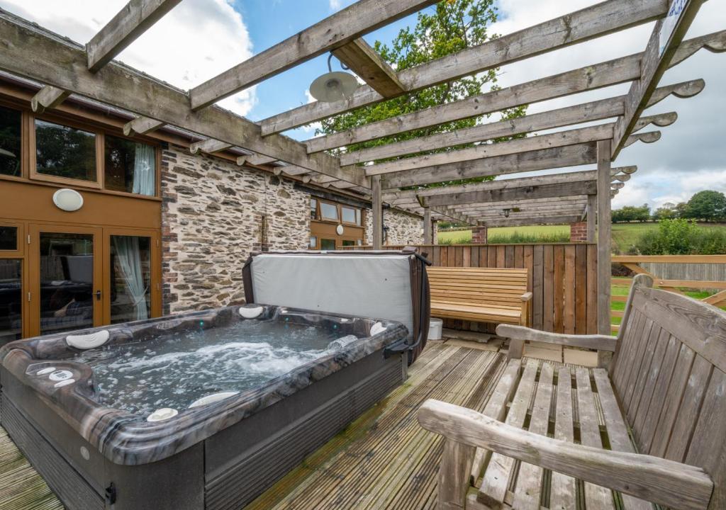 a hot tub on a deck with a bench and a pergola at Hafan Llewelyn in Builth Wells