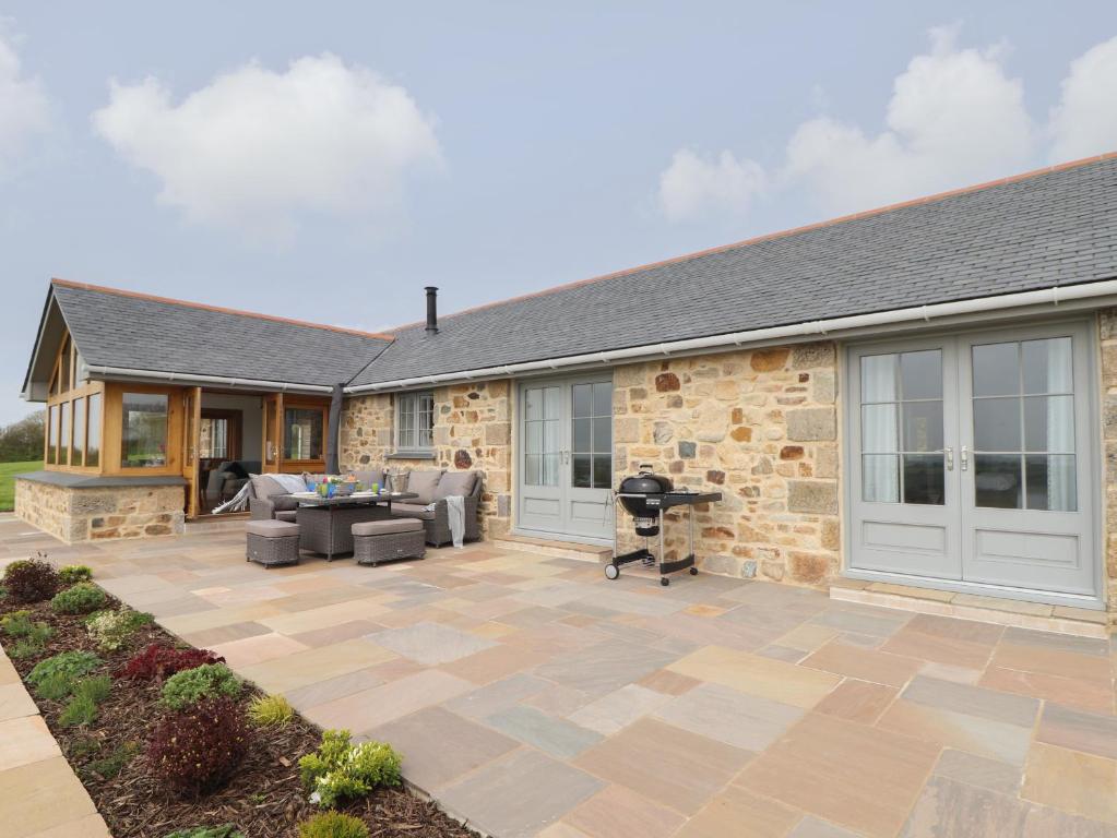 uma casa de pedra com um pátio e um grelhador em Trevilges Cottage em Helston