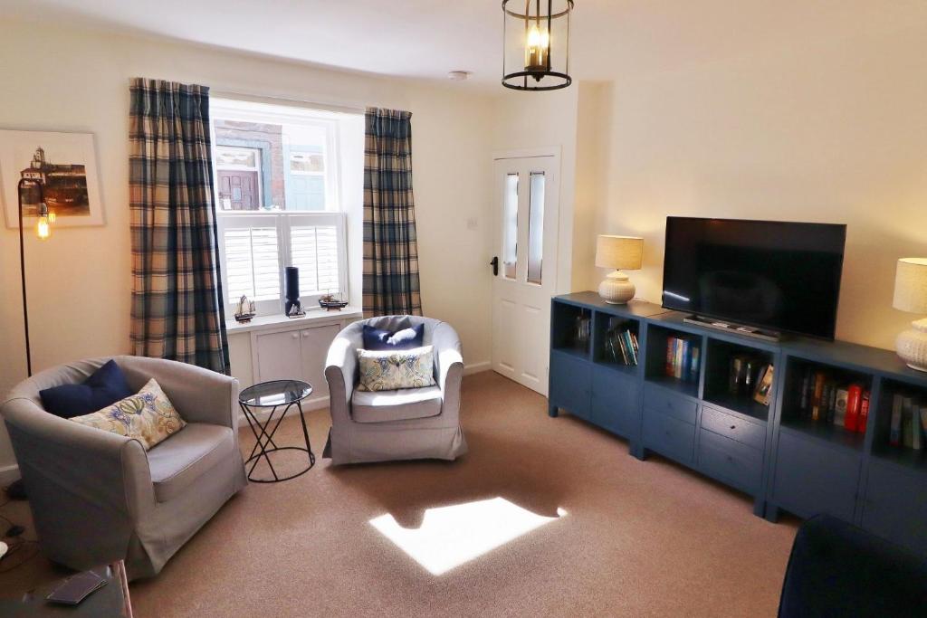 a living room with a tv and a couch and chairs at 14 Union Street in Kirkcudbright