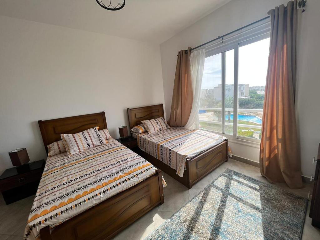 two beds in a bedroom with a large window at شاليه في امواج amwaj in El Alamein
