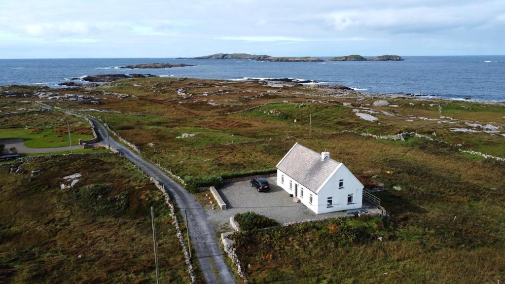a small white house on a hill next to the ocean at Lands End Cottage - Connemara in Aughrus More