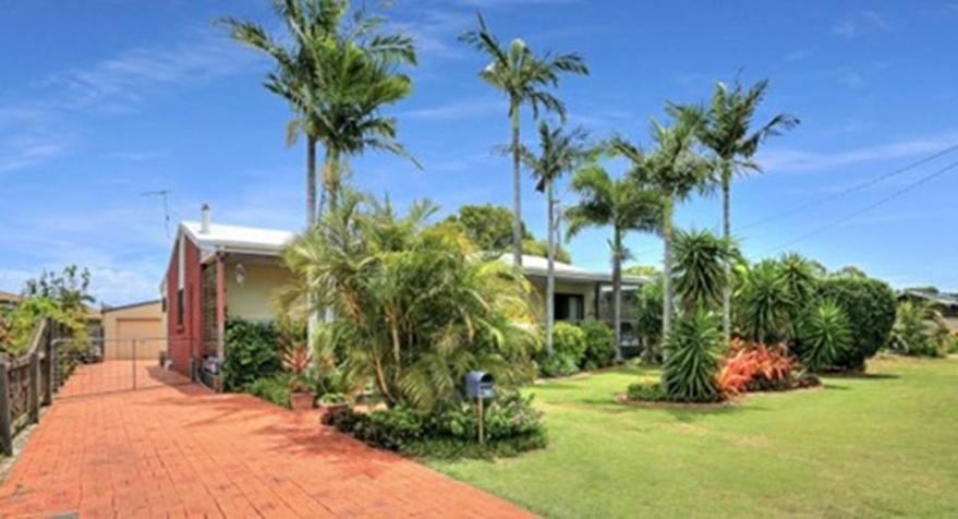 a house with palm trees in front of a yard at Beach Shack in Bargara in Bargara