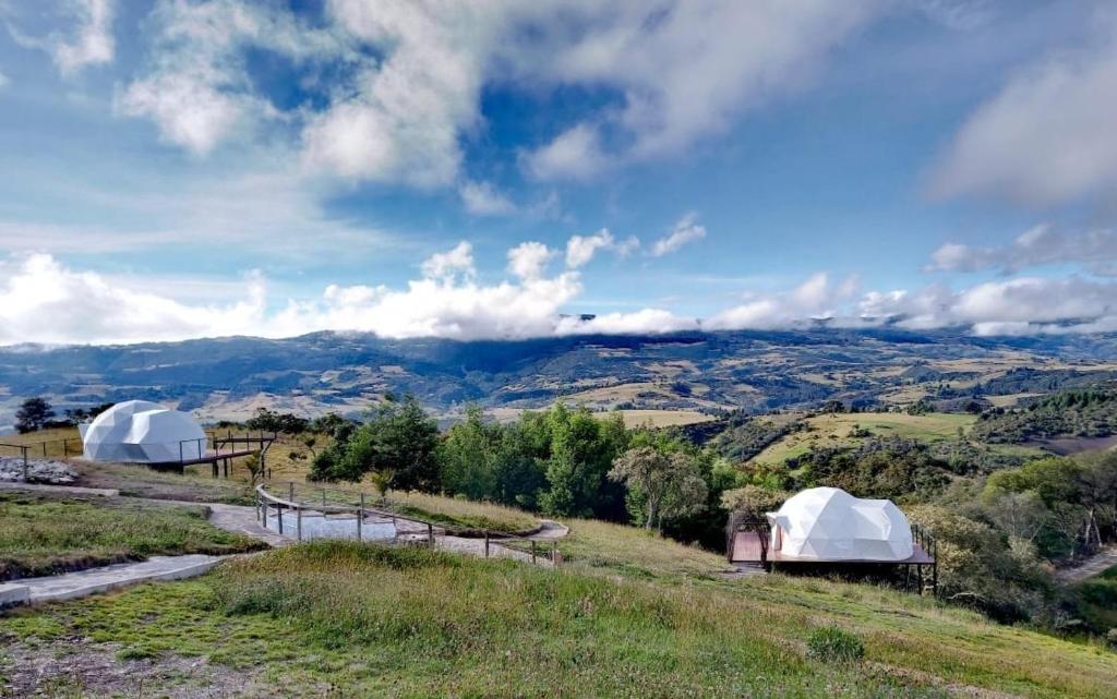 two white domes on a hill with mountains in the background at Glamping Altos De Hayuelos in Paipa