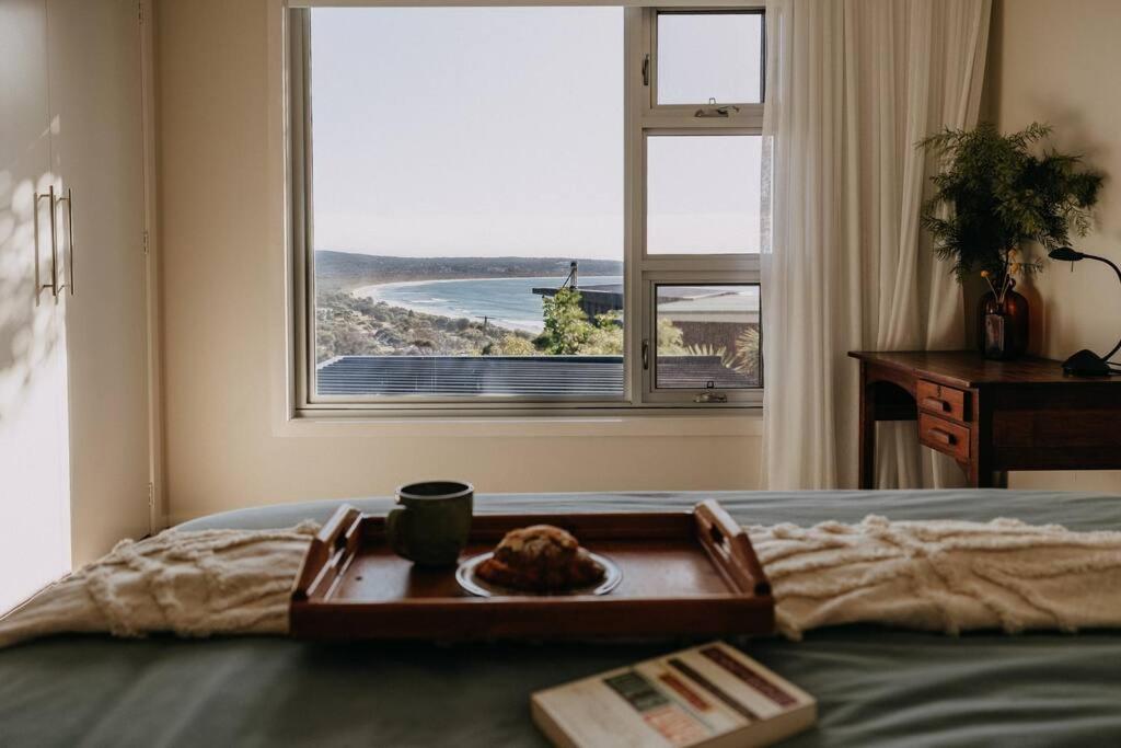 a tray with a plate of food on a bed with a window at Olga and Alma - The Coastal Retreat in Pambula Beach