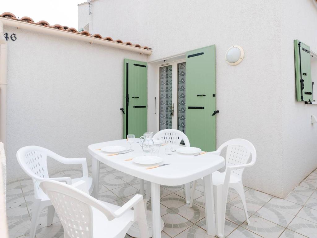 une table blanche avec des chaises blanches et une porte verte dans l'établissement Chaleureuse Villa à Gruissan - 6 pers, Près de la Plage, Garage, Cuisine Équipée, Confort Moderne - FR-1-409A-17, à Gruissan
