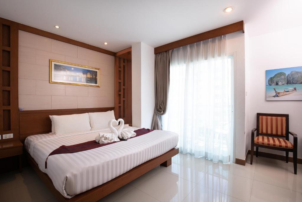 a bedroom with a bed with a window and a chair at The Patong Center Hotel in Patong Beach