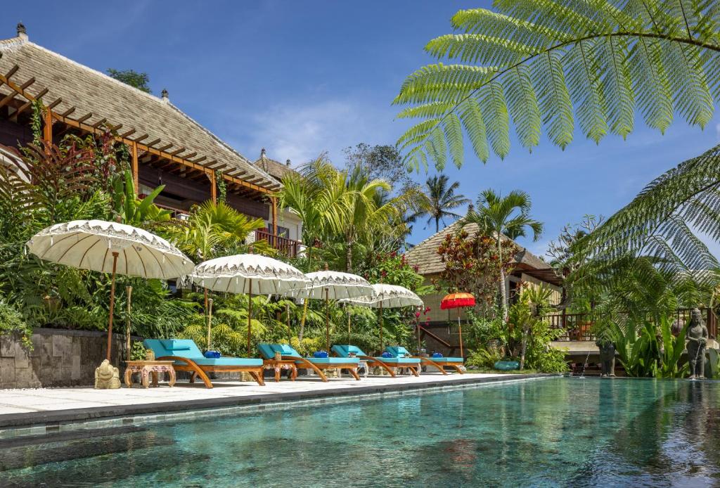 una piscina en un resort con sillas y sombrillas en Villa Lembah Damai by GenuineHost, en Gianyar