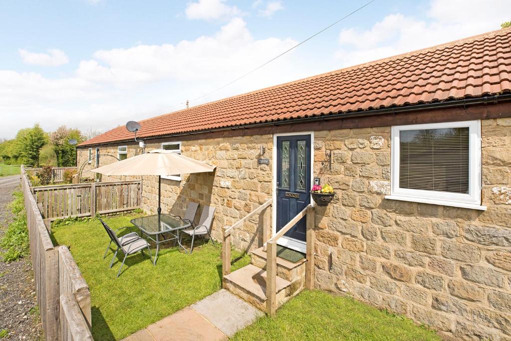 uma casa de pedra com um pátio e um guarda-chuva em Plum Cottage em Knaresborough