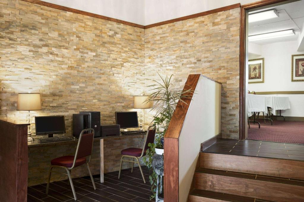 un vestíbulo con 2 escritorios y sillas y una pared de ladrillo en Ramadaby Wyndham Pittsburgh-New Stanton, en New Stanton