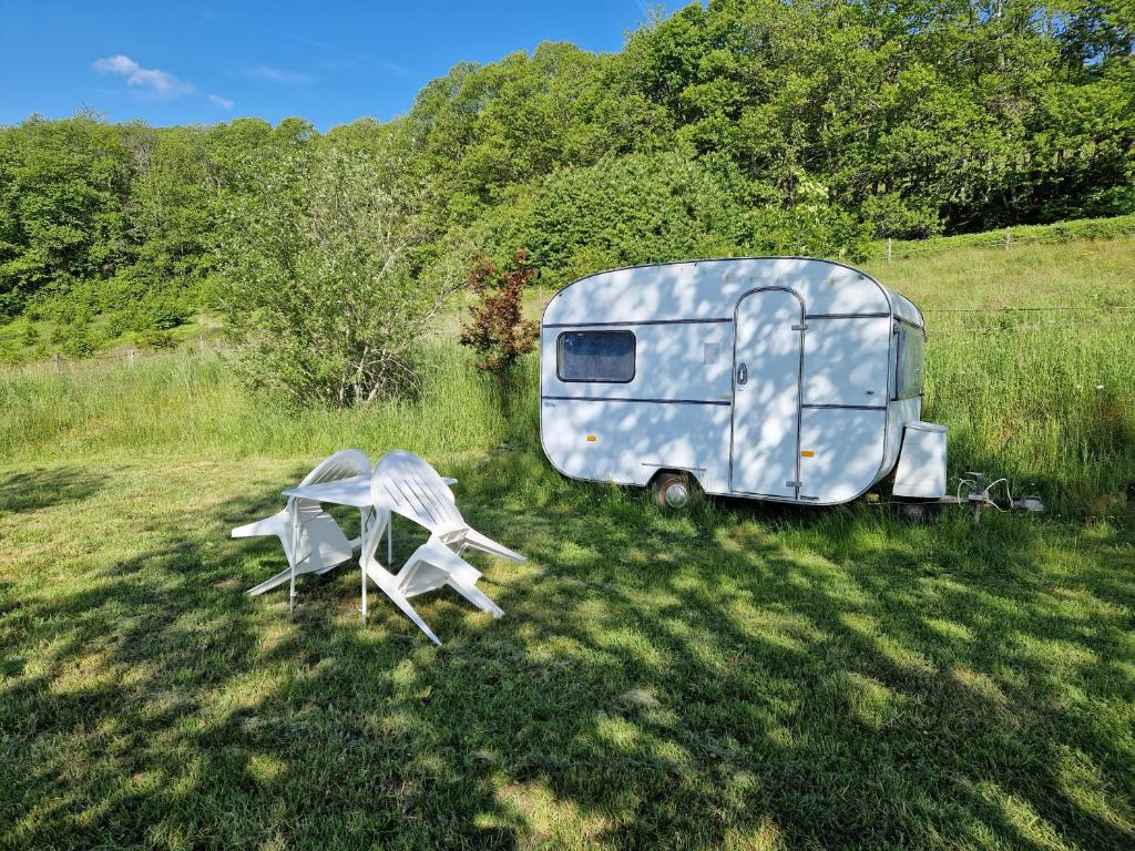 a trailer parked in a field with two chairs at Camping La Fôret du Morvan Vintage caravan in Larochemillay