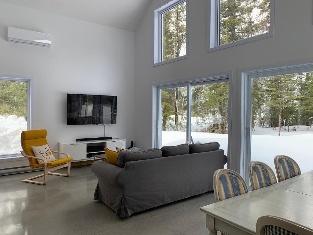 ein Wohnzimmer mit einem Sofa, einem TV und Fenstern in der Unterkunft Le Péribonka in LʼAscension