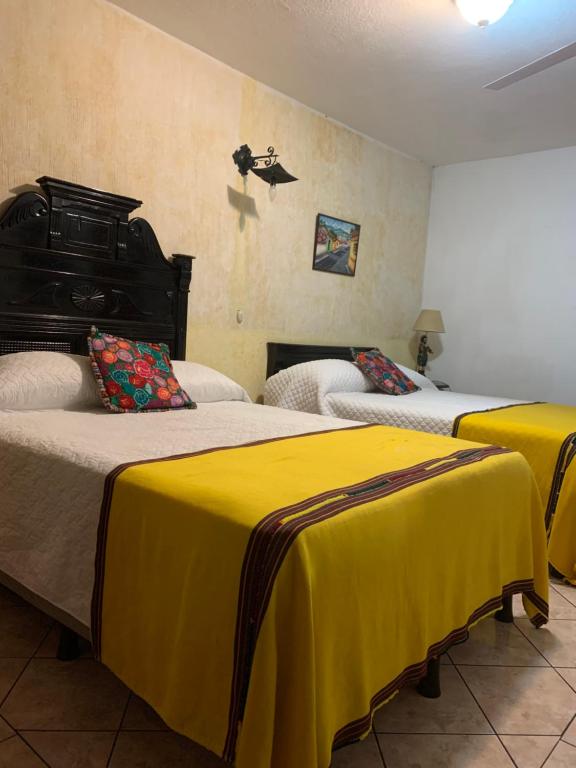 twee bedden in een kamer met gele lakens bij Hotel Posada Don Valentino in Antigua Guatemala