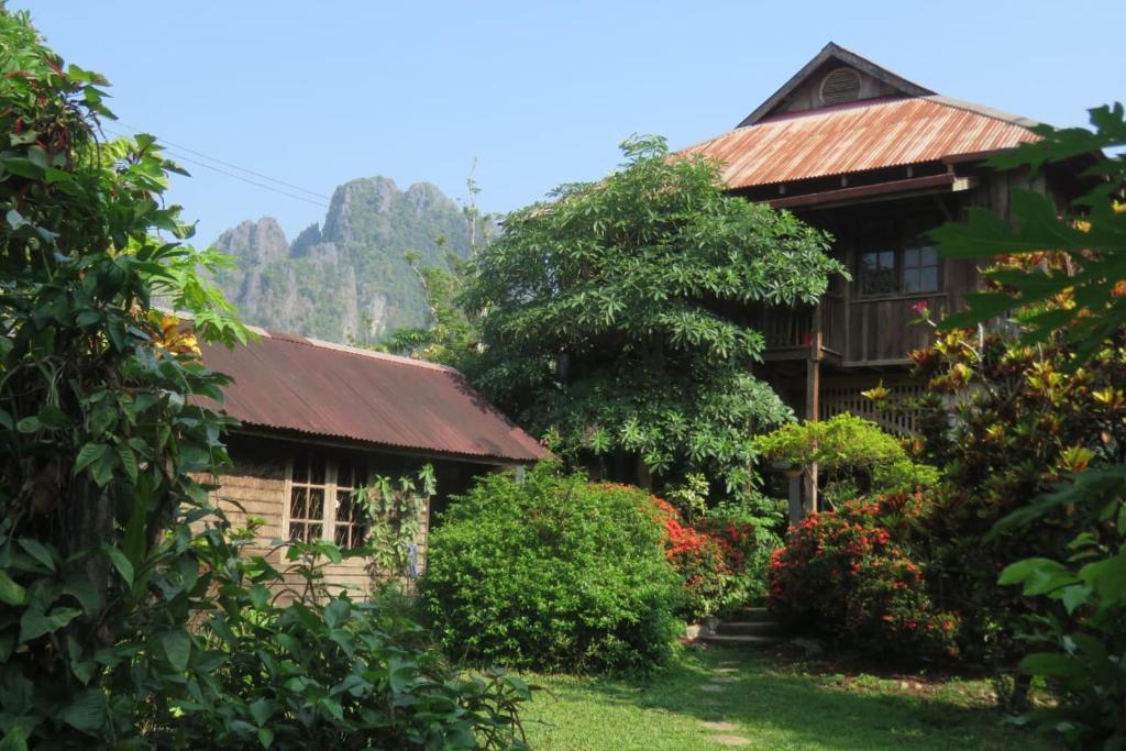 una casa con un techo oxidado y algunos arbustos en Maylyn Guesthouse, en Vang Vieng
