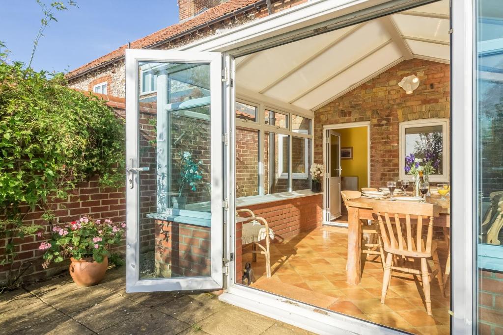 an open sliding glass door to a patio with a table at Plunketts Cottage in Brancaster