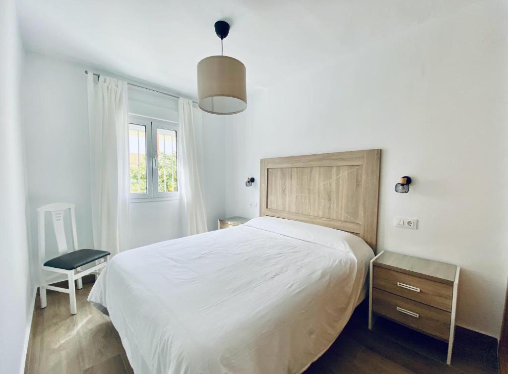 a white bedroom with a large bed and a chair at Apartamentos Turísticos Santo Rostro in Chipiona