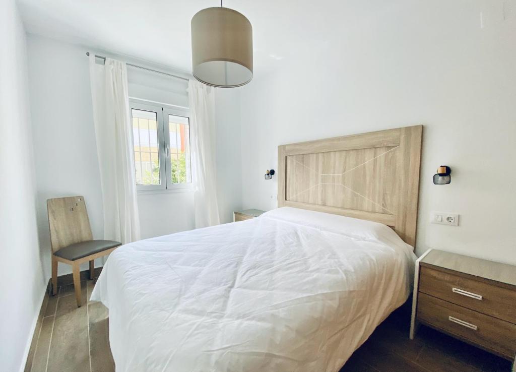 a white bedroom with a large bed and a chair at Apartamentos Turísticos Santo Rostro in Chipiona