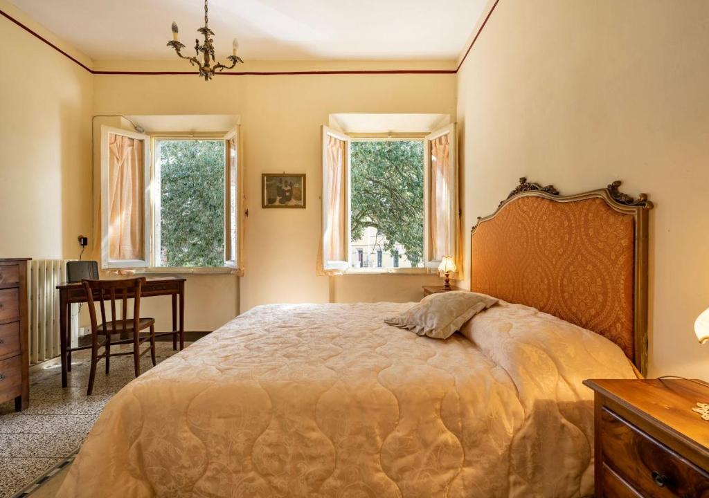 a bedroom with a bed and a table and two windows at 15 min da Montepulciano - Villa Chiara in Montefollonico