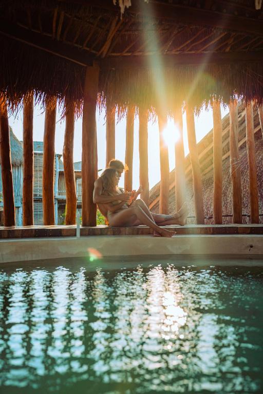 a woman sitting on a porch next to a swimming pool at Hotel Shibari - Restaurant & Cenote Club in Tulum