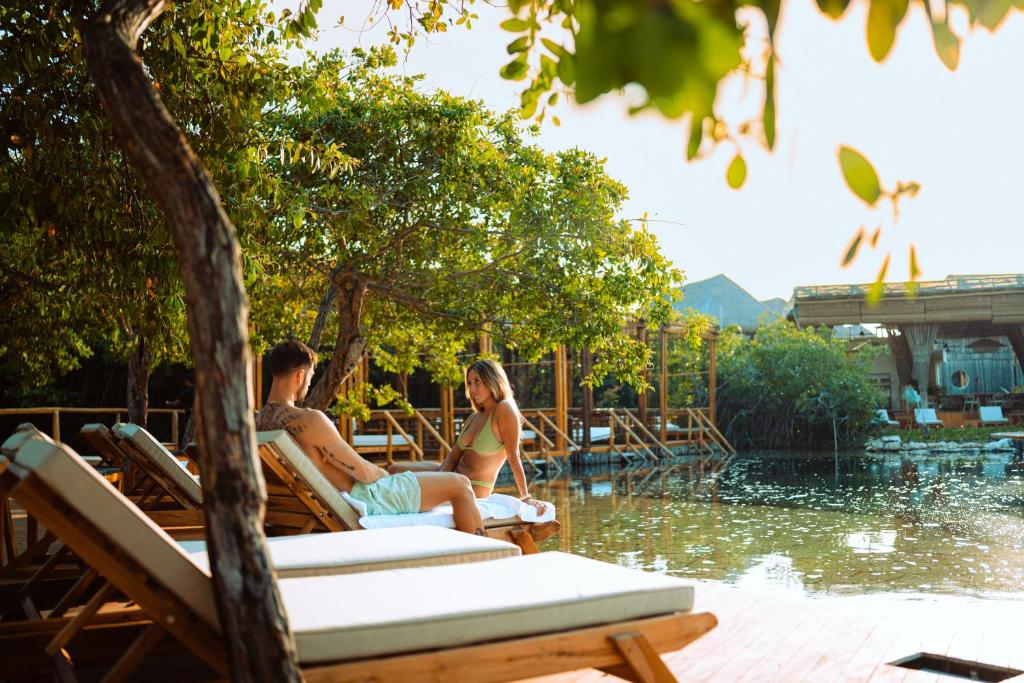 two women sitting on deck chairs by a swimming pool at Hotel Shibari - Restaurant & Cenote Club in Tulum