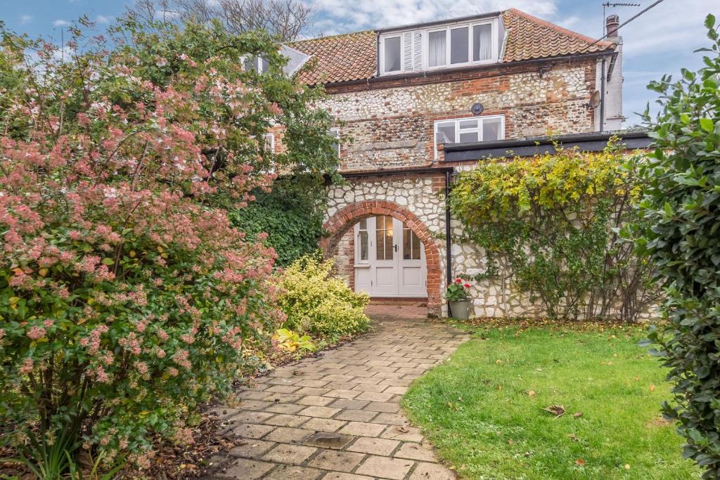 a brick house with a white door and some flowers at The Barn in Burnham Market