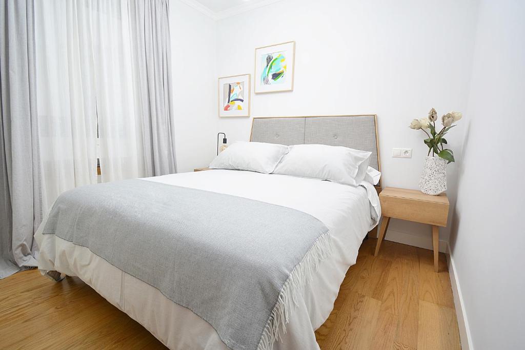 a white bedroom with a large bed and a table at Apartamento frente al mar en Cambados in Cambados