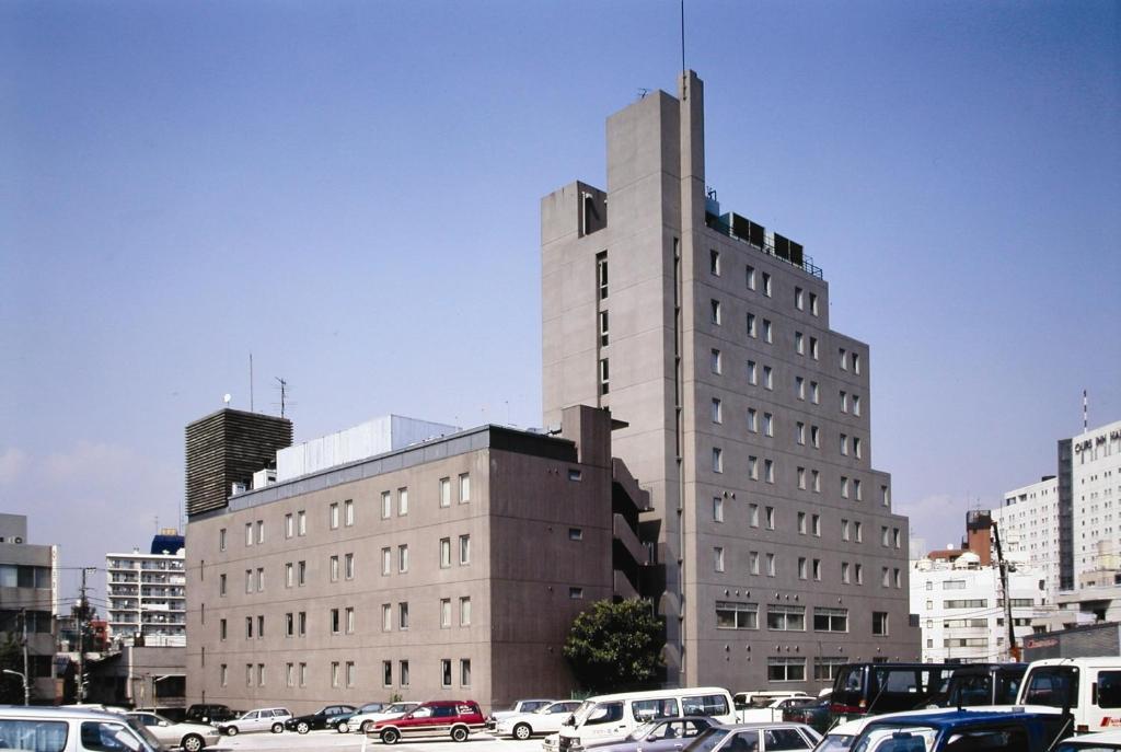 a tall building with cars parked in a parking lot at Hotel Route-Inn Shinagawa-Oimachi in Tokyo